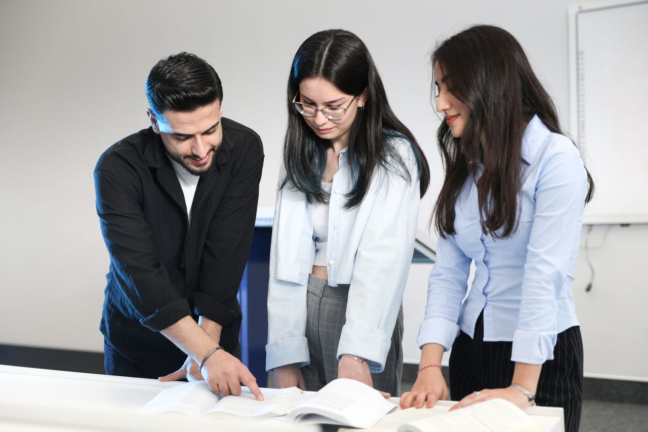 Three young adults discussing and pointing at open documents in a modern office, fostering teamwork.